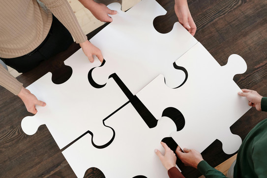 Vier Menschenhände halten vier Puzzleteile
